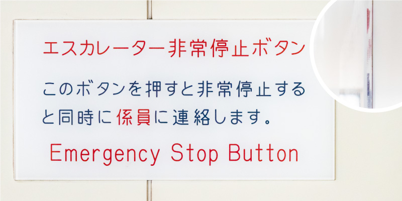 「エスカレーター非常停止ボタン このボタンを押すと非常停止すると同時に係員に連絡します EMERGENCY STOP BUTTON」と書かれた透明・白ふきアクリル板の写真。